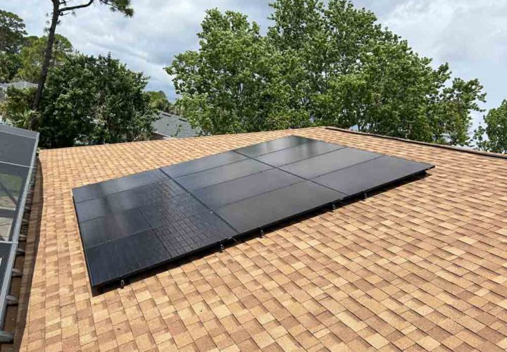 A rooftop view of solar panels installed on a shingle roof. The panels are arranged in a neat grid, capturing sunlight efficiently. The surrounding area features lush green trees, indicating a suburban residential setting. The clean installation highlights the commitment to sustainable energy solutions.