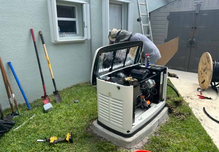 A technician in Melbourne, FL, works on installing a backup generator outside a house. The generator's cover is open, revealing its internal components. Various tools and equipment are scattered around, including shovels, a power drill, and a spool of cable. The installation site is next to a gray house with open windows and a shed in the background.